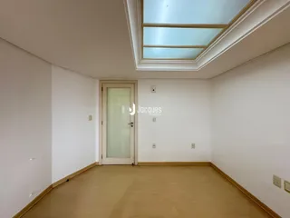 Interior de uma sala com piso de madeira clara e teto com claraboia.