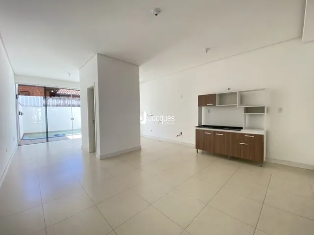 Interior de uma sala ampla com piso claro e paredes brancas.