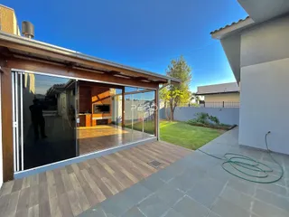 Vista da fachada de uma casa com portas de vidro abrindo para um deck de madeira e jardim.