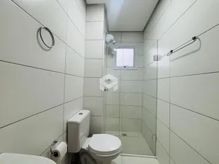 Banheiro com revestimento branco e box de vidro transparente.
