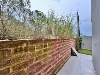 Parede de tijolos com vegetação alta ao fundo.