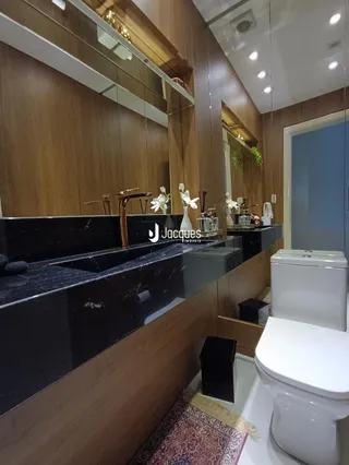 Vista de um banheiro com bancada escura e vaso sanitário branco.