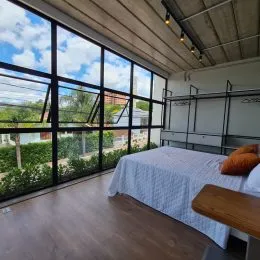 Quarto com cama e grande janela de vidro mostrando a paisagem externa.