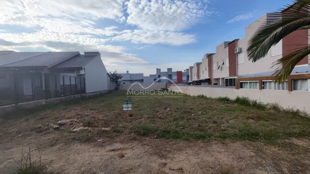 Vista externa de um terreno com vegetação seca em frente a um conjunto de casas residenciais.