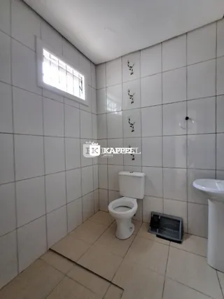 Banheiro com revestimento de azulejos brancos e piso claro.
