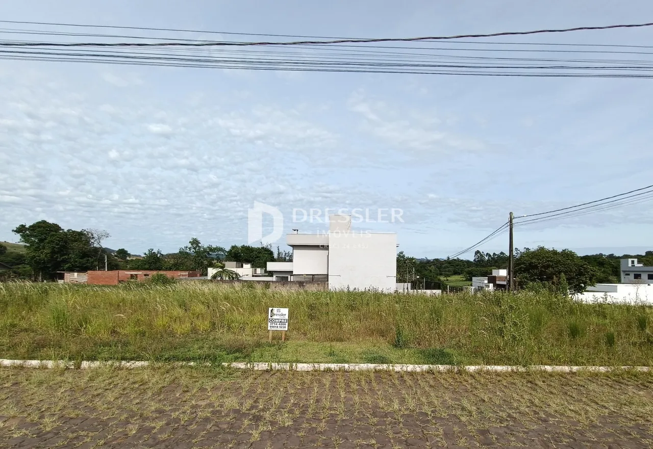 Vista externa de uma propriedade com vegetação e construções ao fundo.