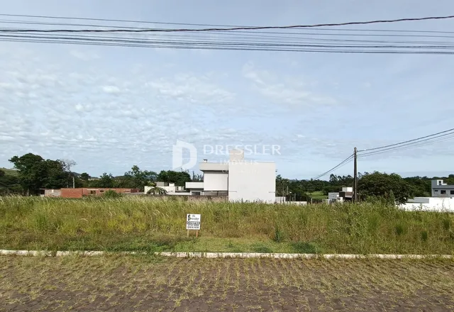 Vista externa de uma propriedade com vegetação e construções ao fundo.