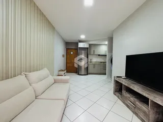 Sala de estar com sofá branco e piso de cerâmica em um apartamento.