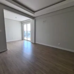 Vista interna de um ambiente com piso de madeira e paredes brancas.