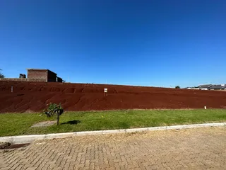 Foto de um terreno com terra vermelha e grama verde sob um céu azul claro.