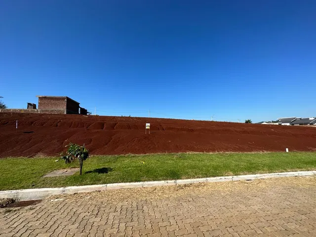 Foto de um terreno com terra vermelha e grama verde sob um céu azul claro.
