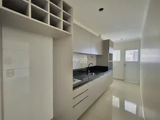Vista interna de uma cozinha moderna com armários brancos e piso claro.