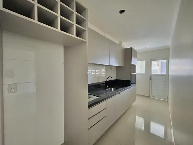 Vista interna de uma cozinha moderna com armários brancos e piso claro.