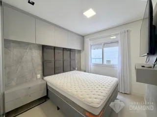 Quarto com cama grande e cabeceira em painel, com janela e cortinas brancas.