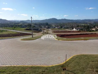 Vista externa de uma área pavimentada com grama e paisagem ao fundo.