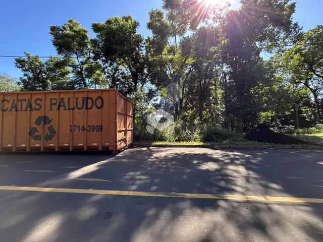 Vista externa de uma propriedade com um contêiner no primeiro plano e vegetação ao fundo.