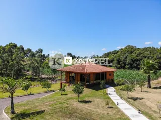Vista externa de uma casa com telhado de telha vermelha cercada por gramado e árvores.