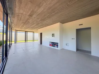 Vista interna de um espaço amplo com teto de concreto e portas de vidro que dão acesso ao exterior.