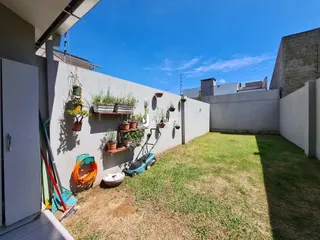 Vista externa de um quintal gramado com muro branco.