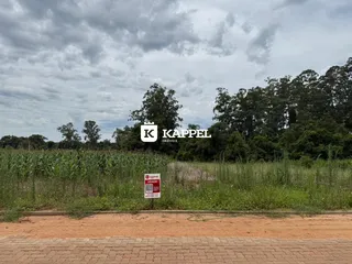 Vista externa de um terreno com vegetação densa e uma placa de venda.