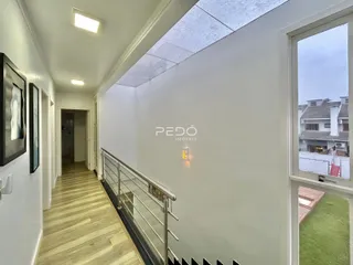 Corredor interno com piso de madeira clara e escada de metal em uma residência.