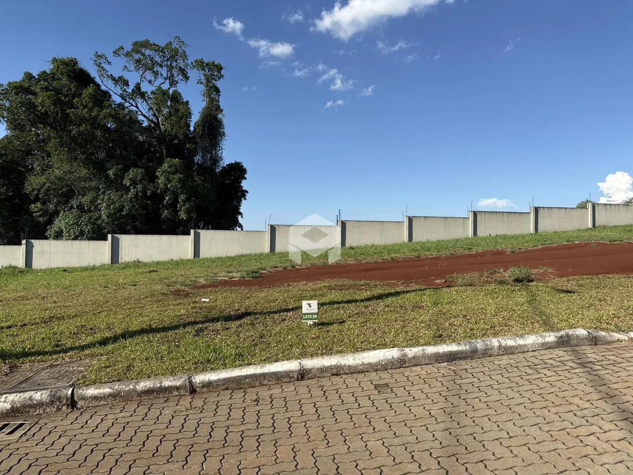 Vista externa de um muro de concreto e área gramada de uma propriedade.