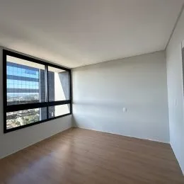 Vista interna de um cômodo com piso de madeira e grande janela.