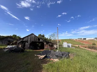 Vista externa de uma estrutura de madeira antiga e deteriorada em um campo aberto.
