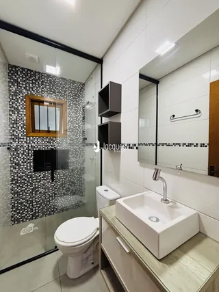 Banheiro com revestimento de azulejos pretos e brancos e box de vidro.