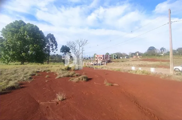 Vista de uma área de terra vermelha e seca com vegetação rasteira sob um céu azul.