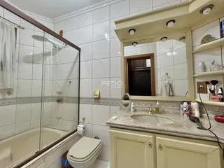 Foto de um banheiro com revestimento cerâmico e box de vidro.