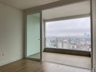 Ambiente interno com piso de madeira e grande janela oferecendo vista para a paisagem urbana.