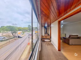 Vista interna de um corredor com teto de madeira e grande janela de uma residência.