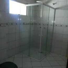 Banheiro com revestimento de azulejos brancos e box de vidro transparente.