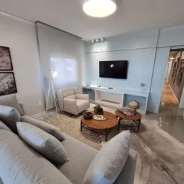 Foto interna de uma sala de estar com sofá e televisão montada na parede.