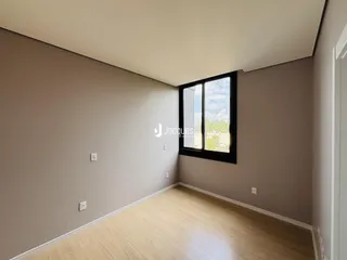 Vista interna de uma sala com piso de madeira clara e grande janela.