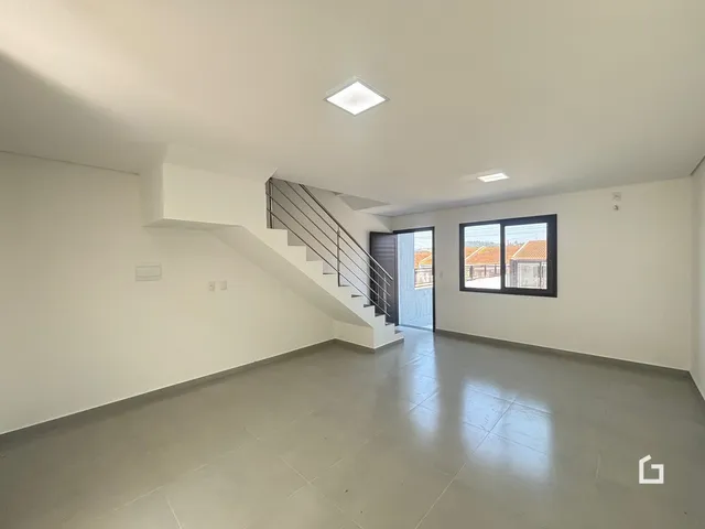 Interior de uma sala com escadaria e piso de concreto.