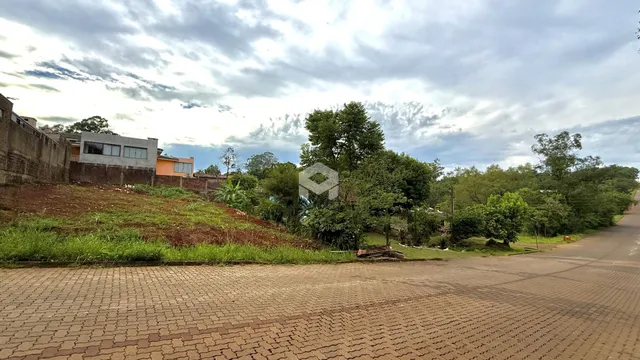 Vista externa de uma propriedade com terreno inclinado e vegetação ao fundo.