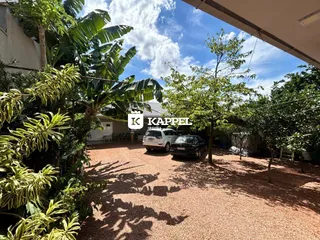 Vista externa do pátio com vegetação e veículos estacionados.