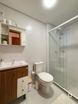 Um banheiro moderno com box de vidro e louças brancas.