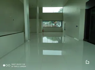 Interior de um corredor amplo com paredes brancas e piso reflexivo.