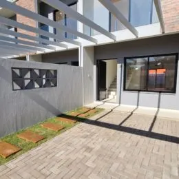 Área externa pavimentada com piso de ladrilhos e vegetação.