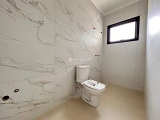 Banheiro com revestimento de mármore e vaso sanitário branco.