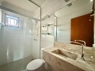 Interior de um banheiro com revestimento cerâmico e box de vidro.