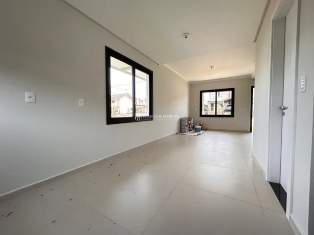 Vista interna de um ambiente amplo com paredes brancas e uma grande janela.