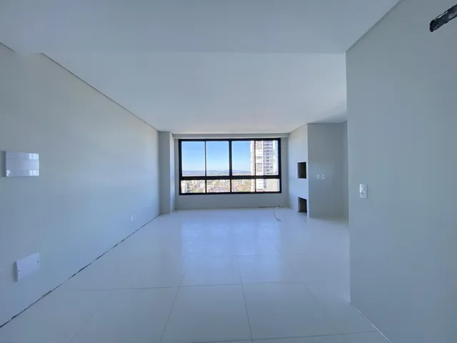 Sala ampla com piso claro e grande janela com vista urbana.