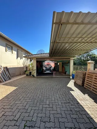 Vista da fachada de uma residência com área coberta e pátio pavimentado.