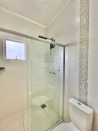 Foto de um banheiro com box de vidro e azulejos brancos.