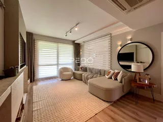 Sala de estar com piso de madeira e grande janela iluminada.