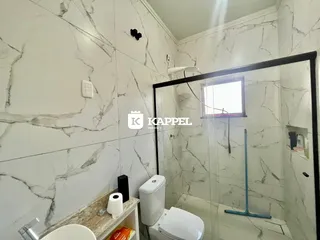 Banheiro com paredes de mármore branco e box de vidro.